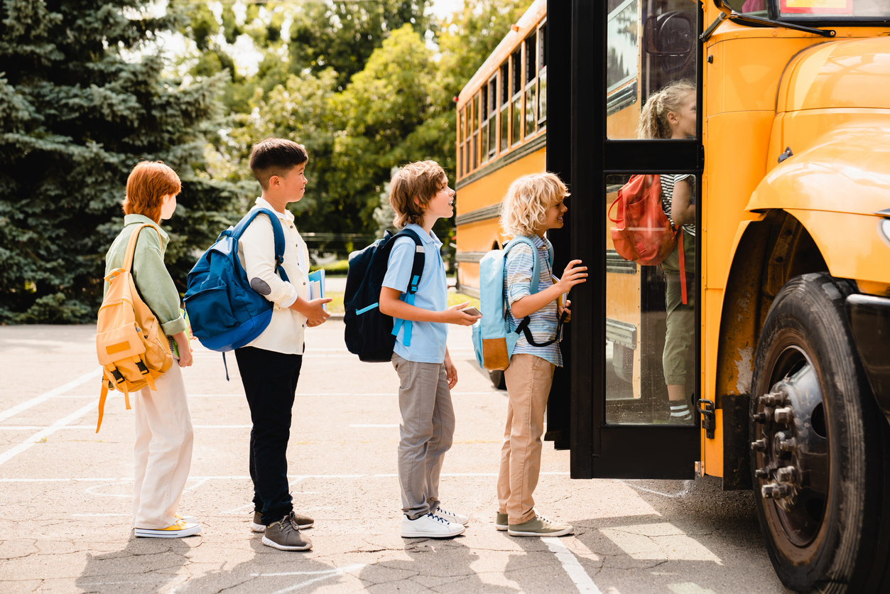 Schoolchildren students standing in line waiting for boarding school bus before starting new educational semester year after summer holidays. (iStock - Inside Creative House)