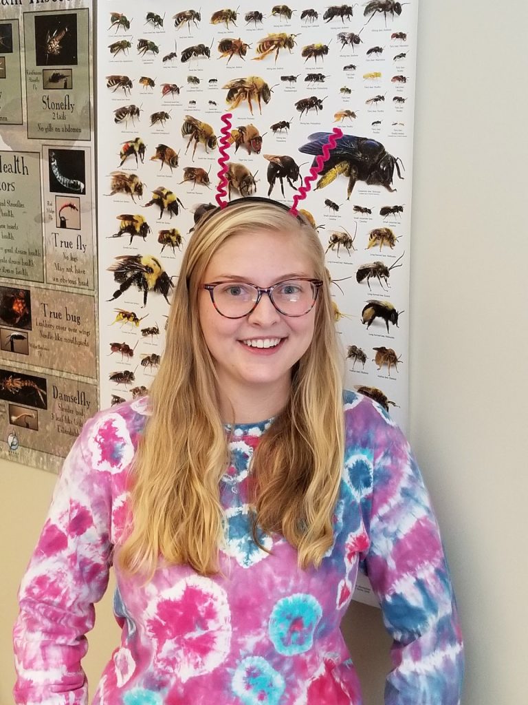 Madison Crawford, who received her bachelor’s and master’s in zoology and physiology from University of Wyoming, poses in front of a bee poster in Lusha Tronstad’s office. Crawford led a study that tested the hypothesis that wind turbine color attracts insects. She was lead author of a paper that was published recently in the journal Western North American Naturalist. (Photo by Lusha Tronstad.)