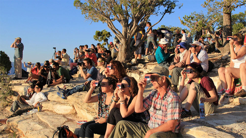 A crowd uses handheld solar viewers and solar eclipse glasses to safely view a solar eclipse. (Credits: National Park Service)