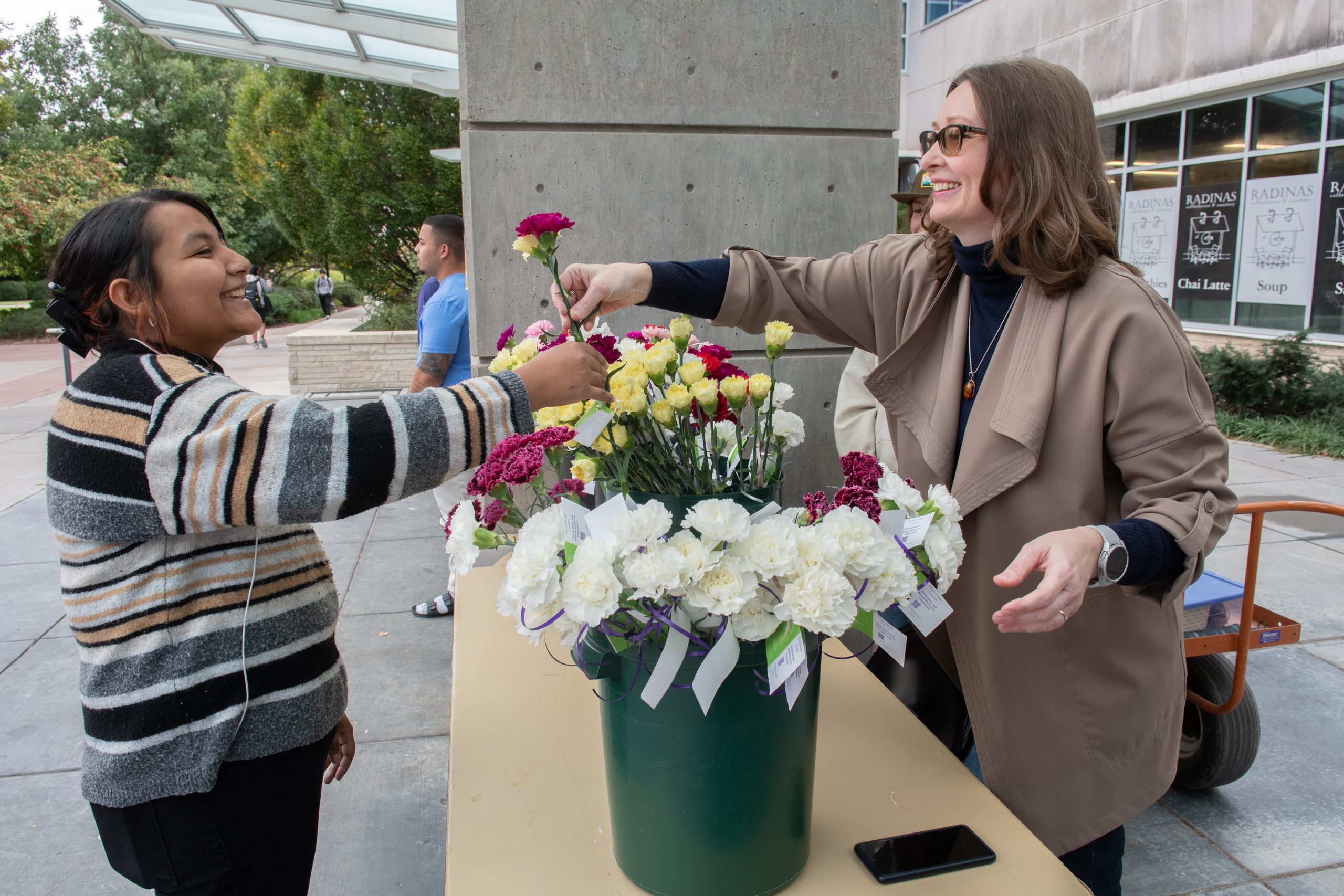 Kansas State University floral design instructor Irina Sheshukova (right) hands two carnations to a college student during the 2023 National Petal it Forward day Oct. 18. (Photo courtesy of K-State Research and Extension.)