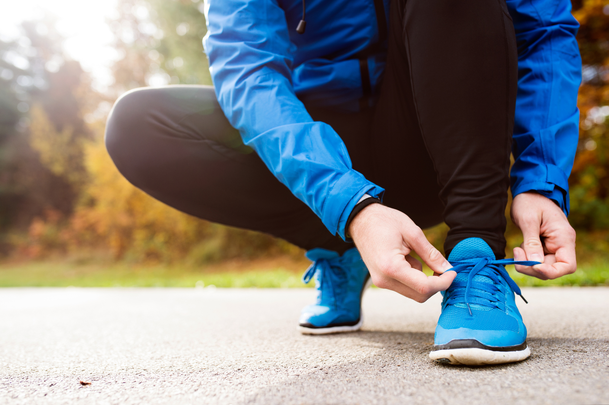 Runner in blue jacket outside in colorful sunny autumn nature, tying shoelaces. (Photo: iStock - Halfpoint)