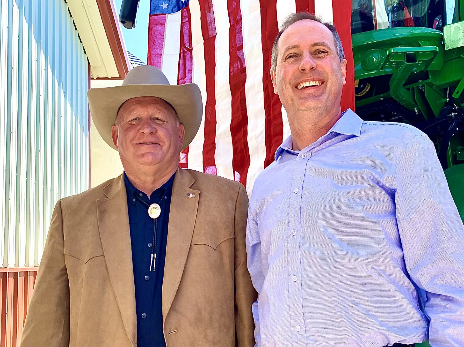 U.S. Reps. Glenn “GT" Thompson, R-PA, chairman of the House Agriculture Committee, left, and Tracey Mann, R-KS, pose for photos in front of a patriotic backdrop May 2, after the Kansas Food & Agriculture Listening Session in a farm shop north of Gypsum, Kansas (Photo by Tim Unruh.)