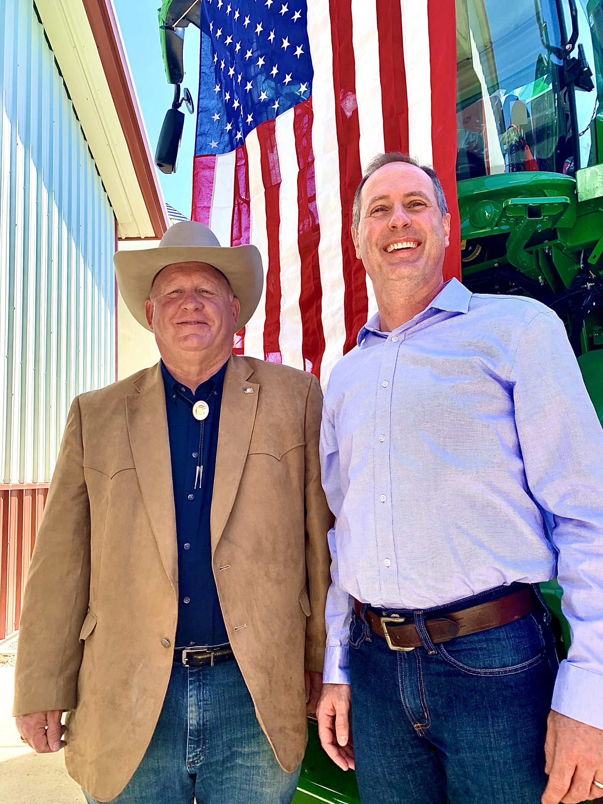 U.S. Reps. Glenn “GT" Thompson, R-PA, chairman of the House Agriculture Committee, left, and Tracey Mann, R-KS, pose for photos in front of a patriotic backdrop May 2, after the Kansas Food & Agriculture Listening Session in a farm shop north of Gypsum, Kansas (Photo by Tim Unruh.)
