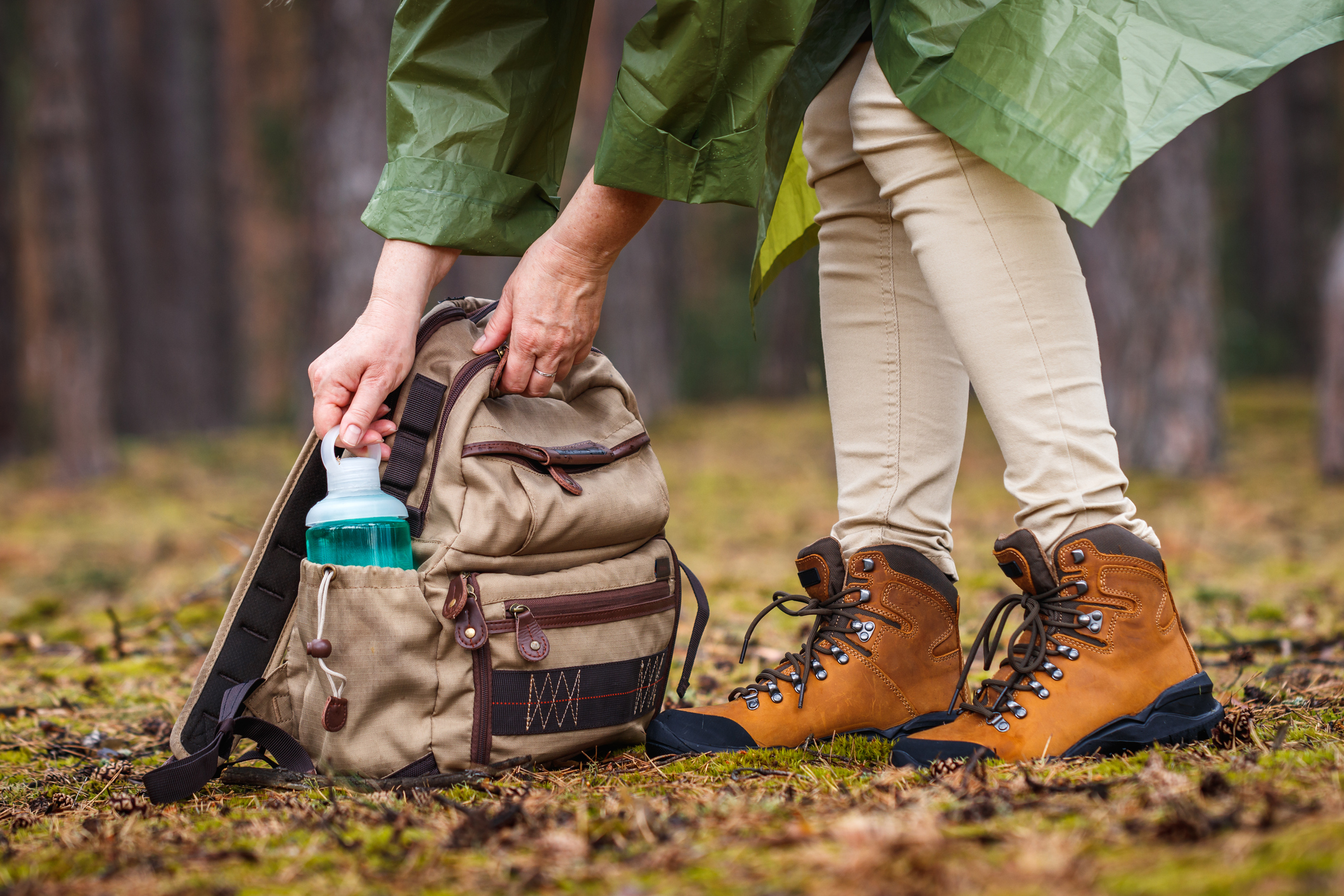 Woman with raincoat and hiking boots taking out water bottle from backpack. Refreshment during hike in forest (Photo: iStock - Zbynek Pospisil)