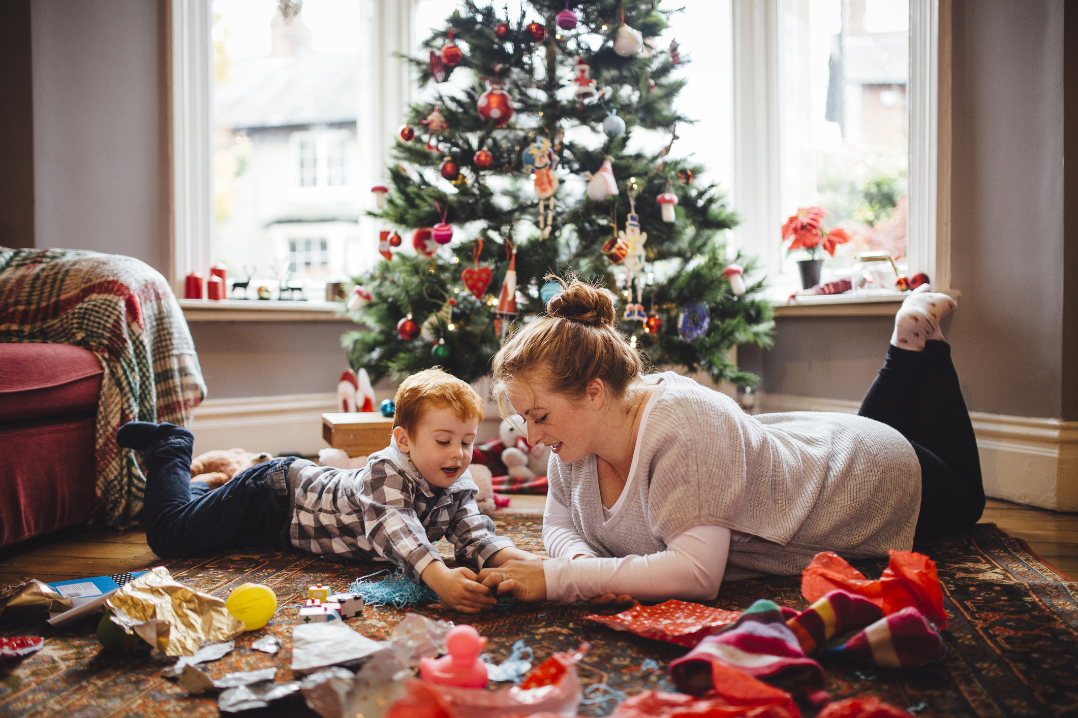 A young mother and her son are celebrating Christmas morning together, they are both lying on the floor and playing with newly opened toys together. (Photo: iStock - SolStock)