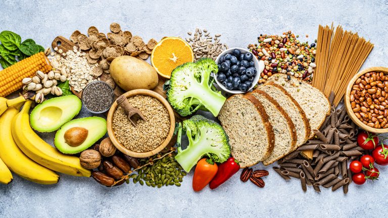 Overhead view of a large group of food with high content of dietary fiber arranged side by side. The composition includes berries, oranges, avocado, chia seeds, wholegrain bread, wholegrain pasta, whole wheat, potatoes, oat, corn, mixed beans, brazil nut, sunflower seeds, pumpkin seeds, broccoli, pistachio, banana among others. (Photo: iStock - fcafotodigital)