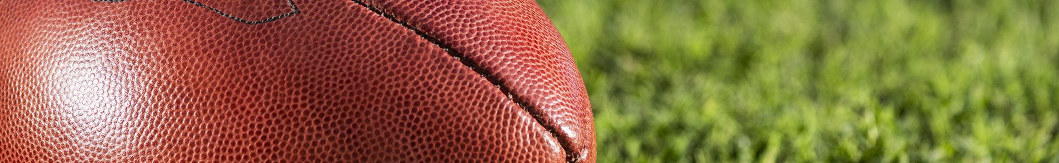A low angle close-up view of a leather American Football sitting in the grass next to a white yard line with hash marks in the background. (Photo: iStock - cmannphoto)