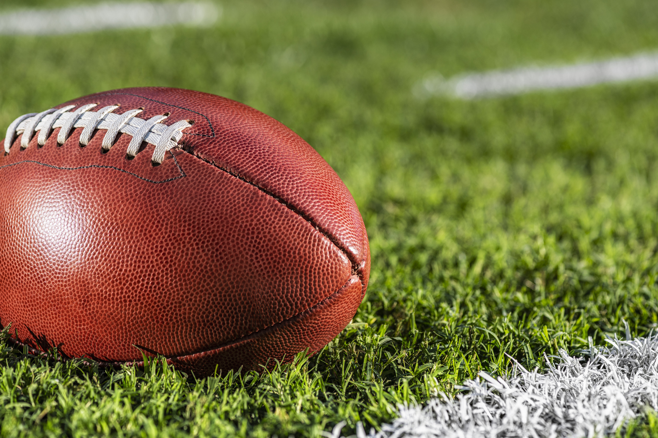 A low angle close-up view of a leather American Football sitting in the grass next to a white yard line with hash marks in the background. (Photo: iStock - cmannphoto)
