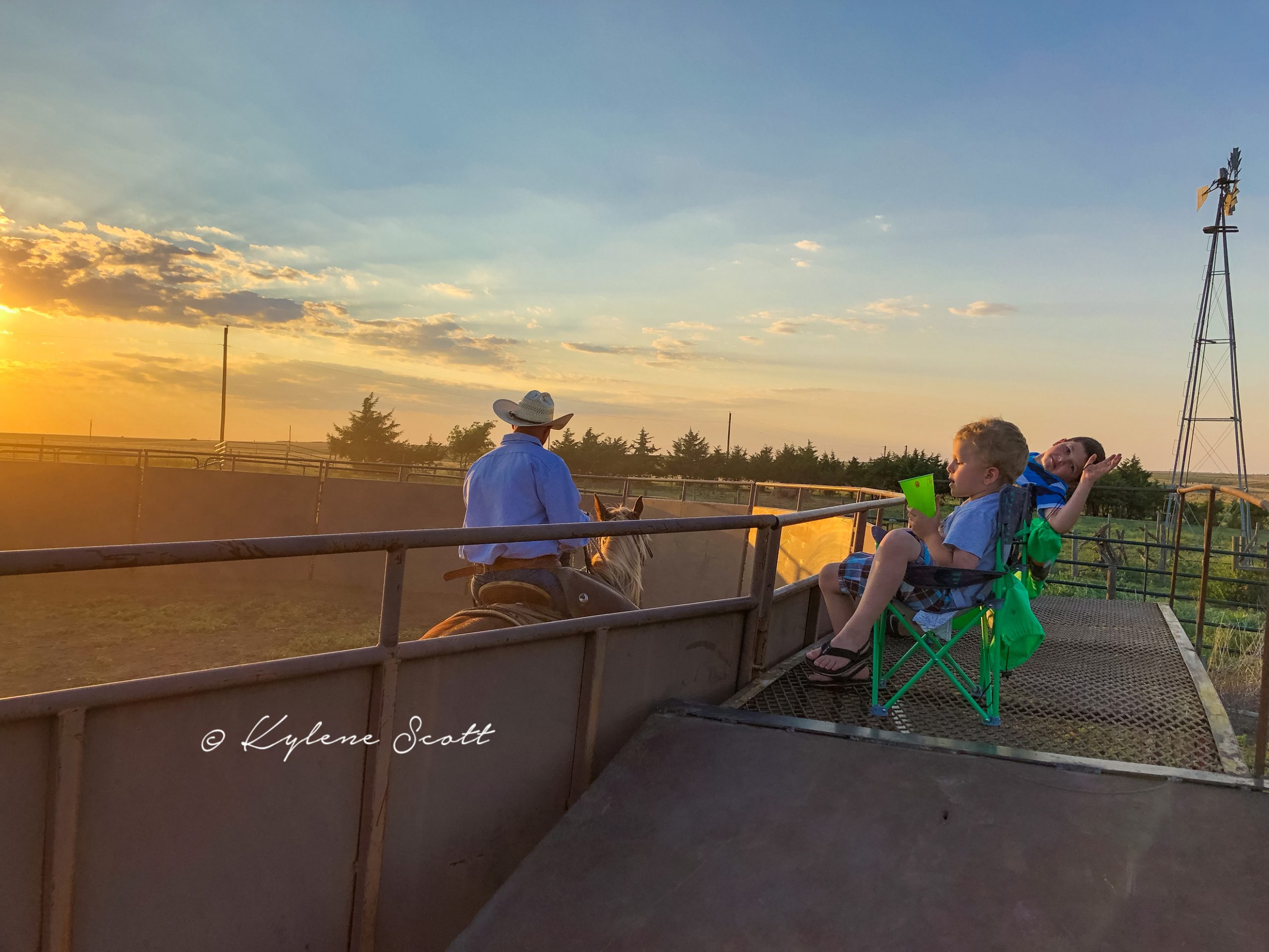 My boys watch their Dad ride a horse on a summer evening in 2018. They're too distracted to get anything from his sessions. (Journal photo by Kylene Scott.)