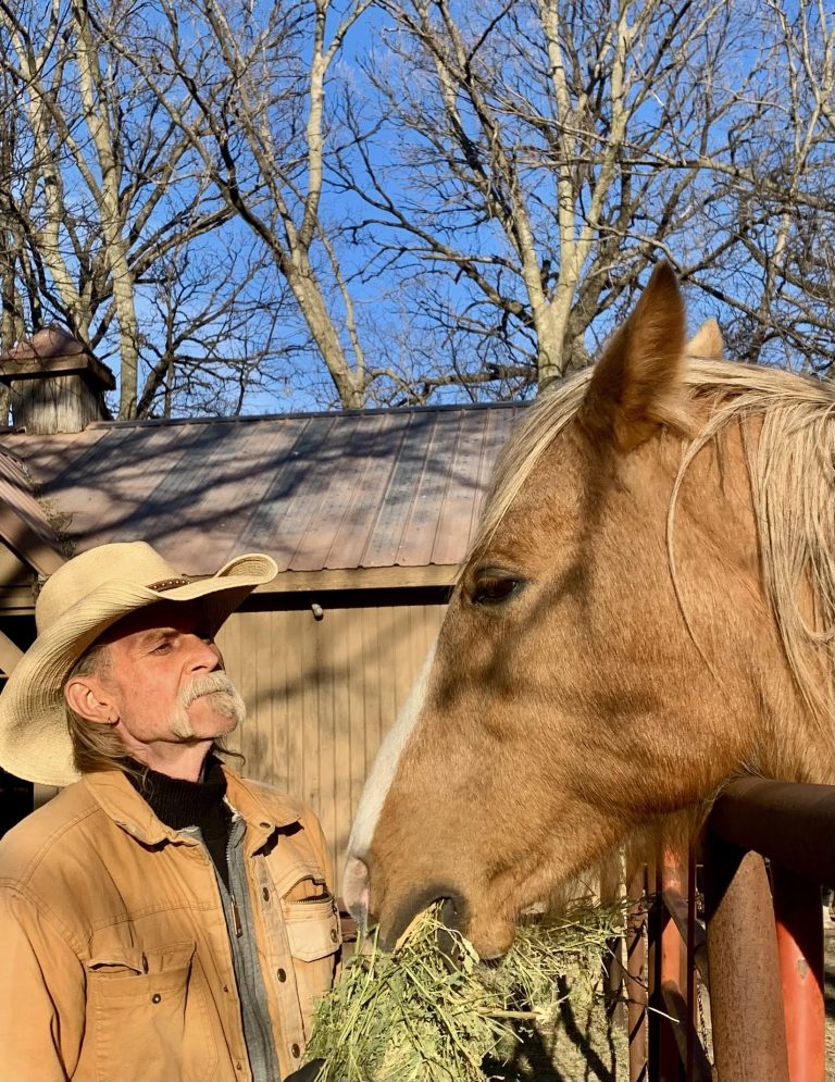 Duane Scoville of Solomon, Kansas, presents a tuft of leafy alfalfa hay to his horse, Paloma. (Photo by Tim Unruh.)