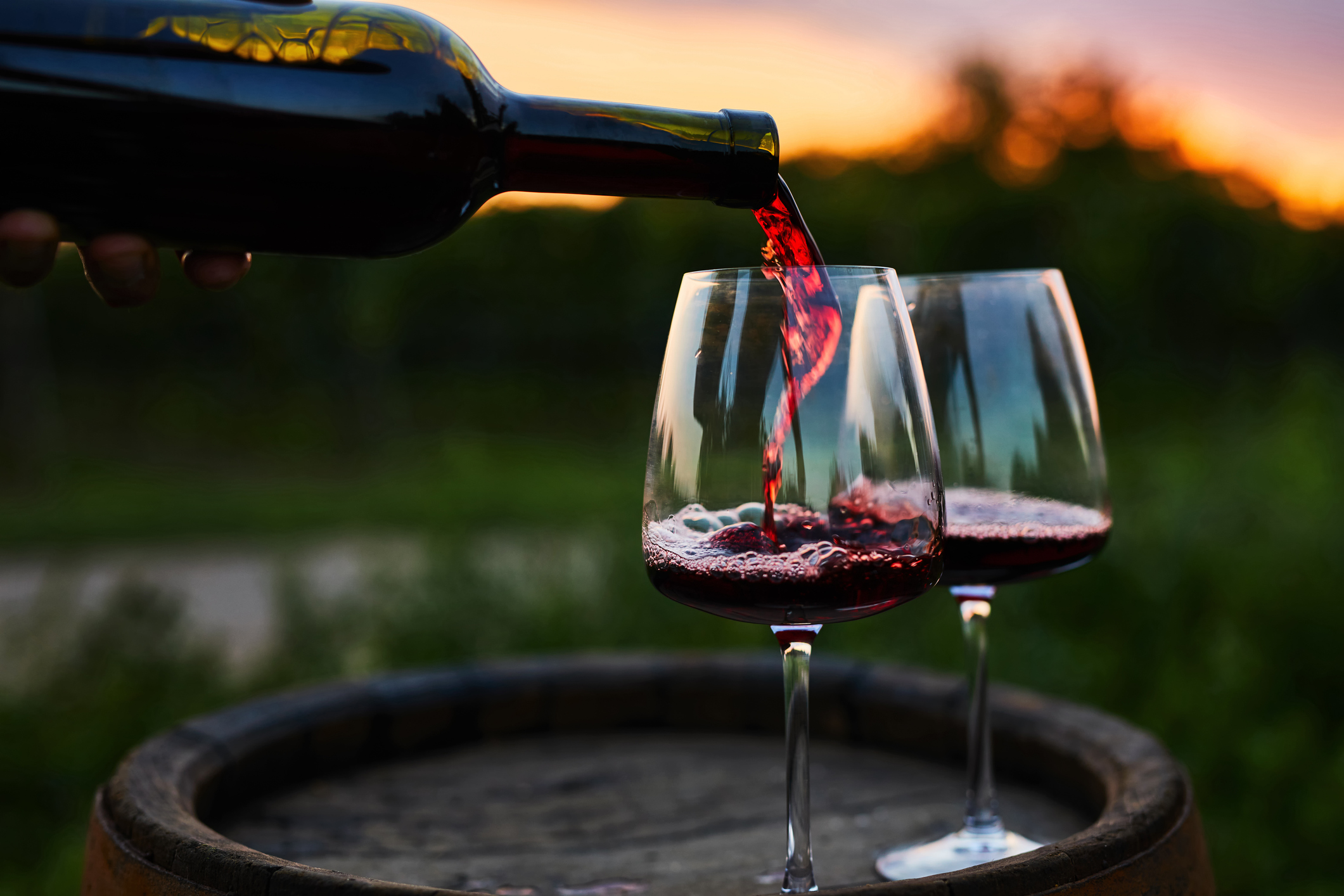 Pouring red wine into glasses on the barrel at dusk (Photo: iStock - Rostislav_Sedlacek)