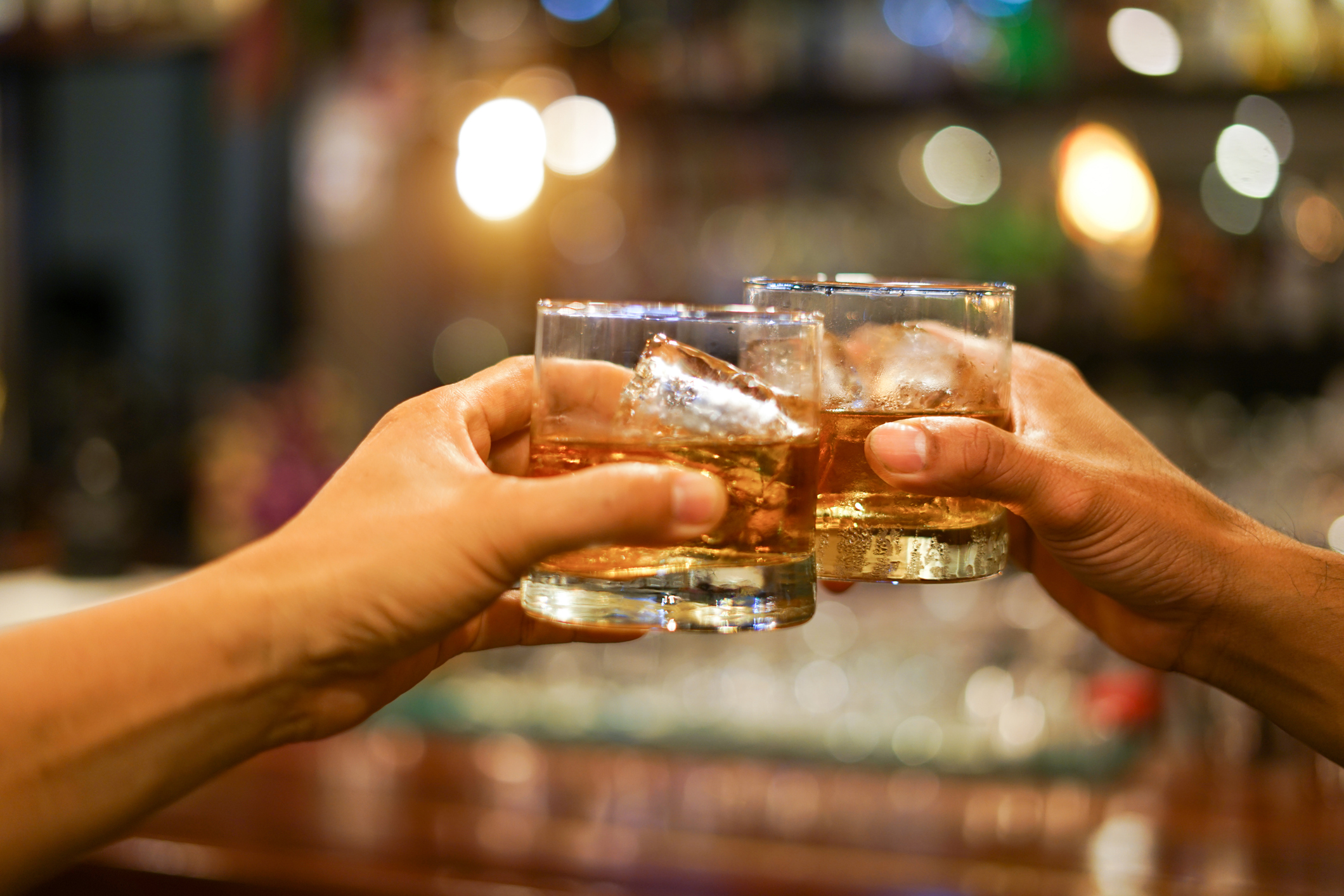 Two men clinking glasses of whiskey drink alcohol beverage together at counter in the pub (Photo: iStock - krisanapong detraphiphat)