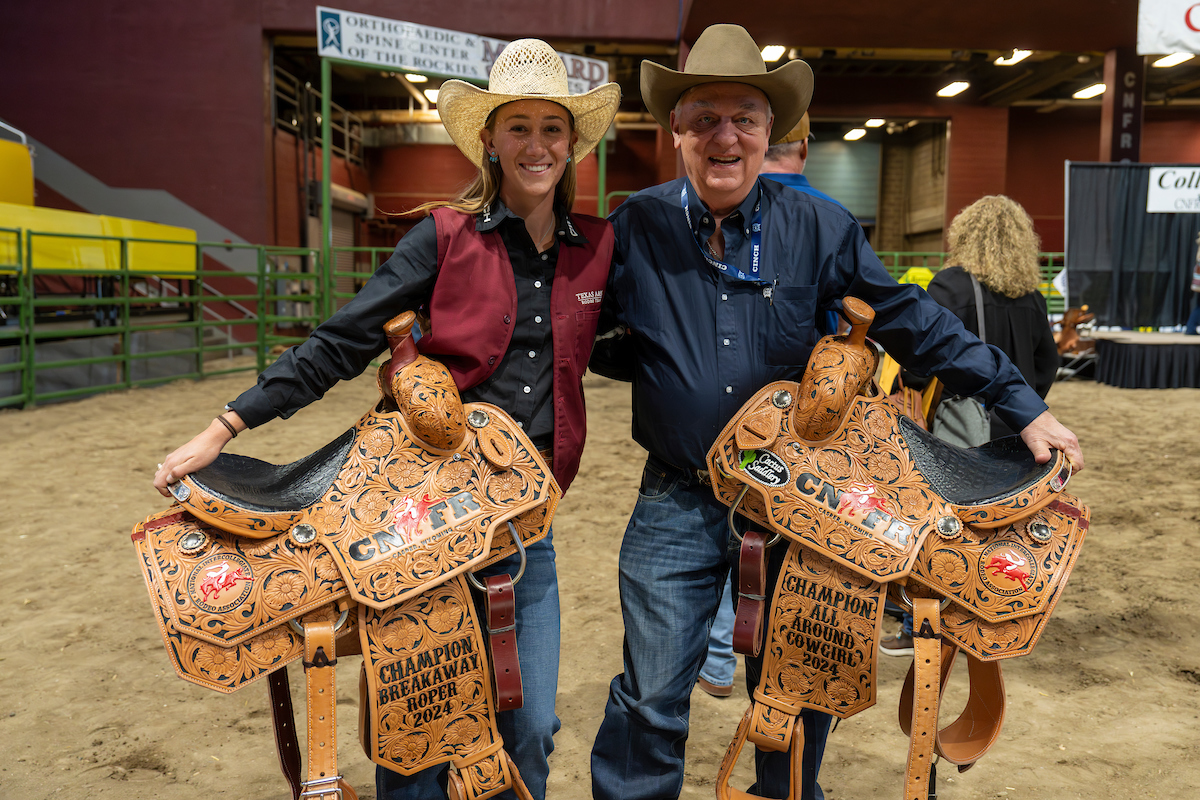Madalyn Richards ’25, of Hereford, collects her champion saddles with Aggie Rodeo coach Al Wagner, Ph.D., after being named the 2024 Breakaway Roping Champion and earning the 2024 Women’s All-Around title during College National Finals Rodeo in Casper, Wyoming. (Michael Miller/Texas A&M AgriLife)