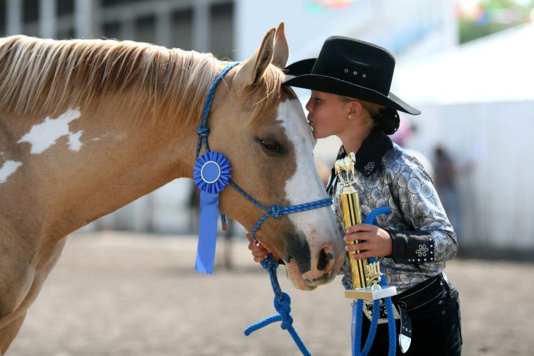 Cowgirl contestant holding her ribbons she won with her horse in an arena during fair (Photo: iStock - BrandyTaylor)
