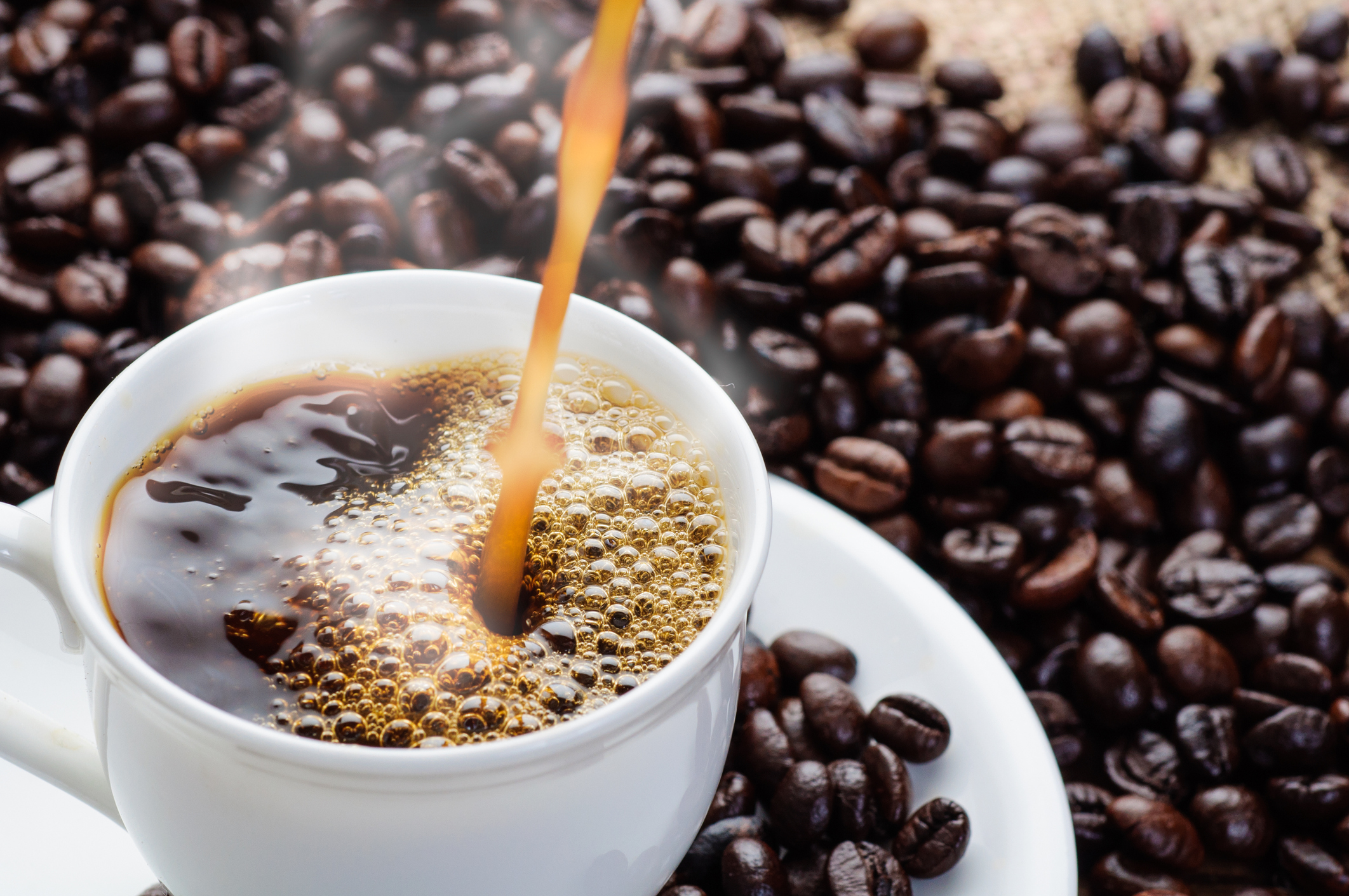 coffee pouring to cup surrounded by coffee beans (Photo: iStock - iWichy)