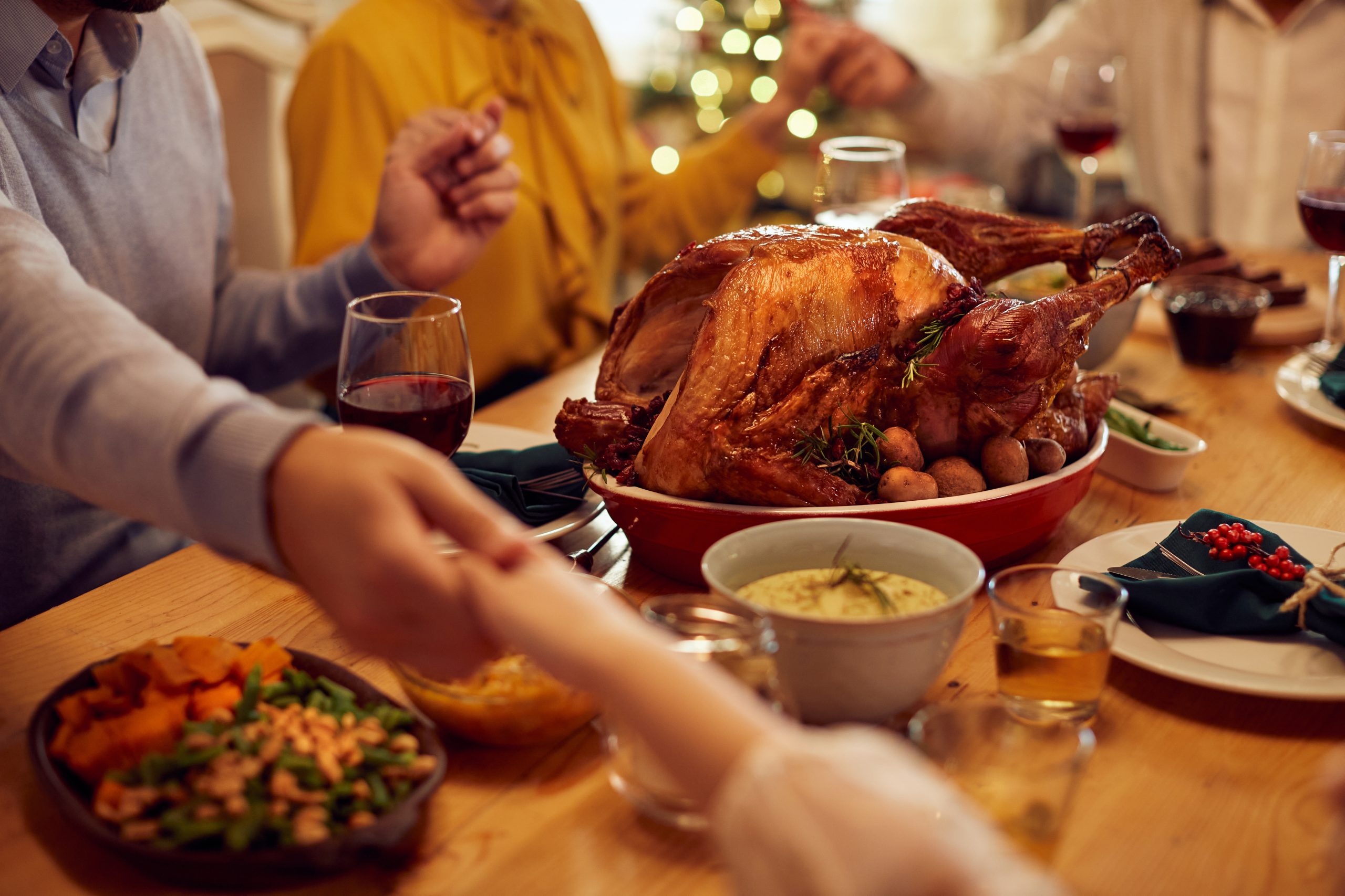 Close-up of family saying grace while holding hands during Thanksgiving meal at dining table. (Photo: Adobe Stock │ #465695788 - Drazen)