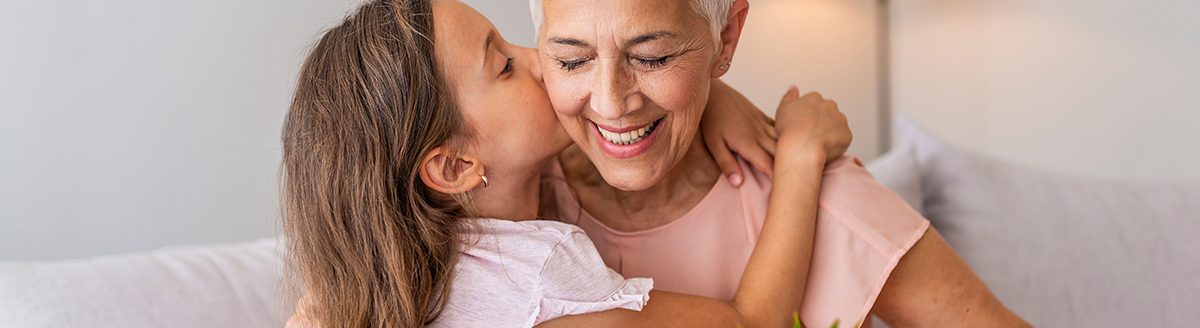 Little preschool granddaughter kissing happy older grandma on cheek, giving sunflower. (Photo: Adobe Stock │ #284777270 - Dragana Gordic)