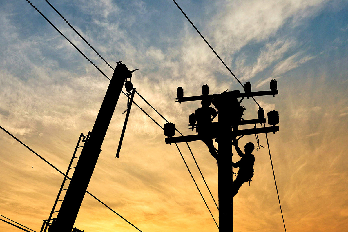 Silhouette electricians team with crane are working to install electrical transmission equipment on power pole (Photo: Adobe Stock │ #253451746 - Prapat)