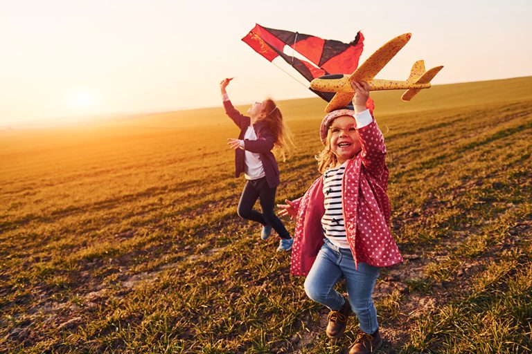 Two little girls friends have fun together with kite and toy plane on the field at sunny daytime. (Adobe Stock │ #369531968 - standret)