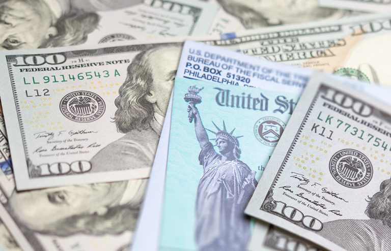 United States IRS check and envelope resting on money. (Adobe Stock │ #402728861 - Andy Dean)