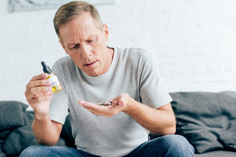 Man in t-shirt holding pills and cannabis oil. (Adobe Stock │ #291199705 - LIGHTFIELD STUDIOS)