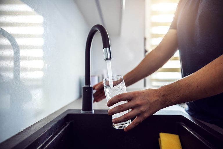 Young man pouring fresh water from kitchen sink. (Adobe Stock │ #342993736 - Dusan Petkovic)