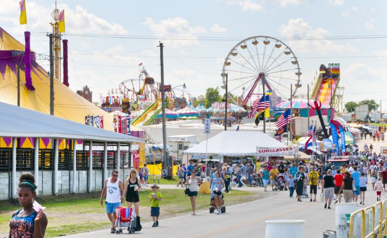Sedalia, Missouri, United States - August 13, 2011: Fairgoers crowd the road at the Missouri State Fair. A ferris wheel, roller coaster, a giant slide, and livestock pavilions are included in the festivities. (iStock │ #458610387 - Lokibaho)