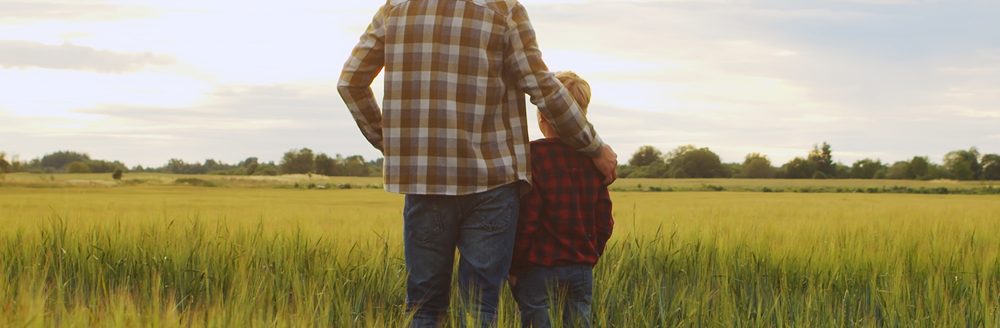 Farmer and his son in front of a sunset agricultural landscape. (Adobe Stock │ #530362856 - Acronym)