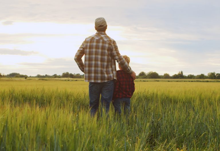 Farmer and his son in front of a sunset agricultural landscape. (Adobe Stock │ #530362856 - Acronym)