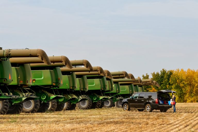 Many combine harvester machines in a row on agriculture farm with woman standing by her car and taking out some stuff. (iStock │ #1895288797 - AJ_Watt)