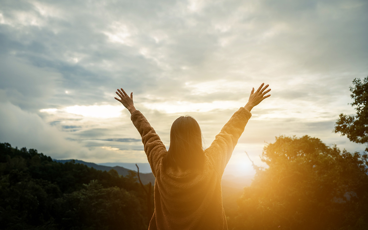 Happy woman on the sunset in nature in winter with arm raised and open hand. (Adobe Stock │ #389782088 - Monster Ztudio)