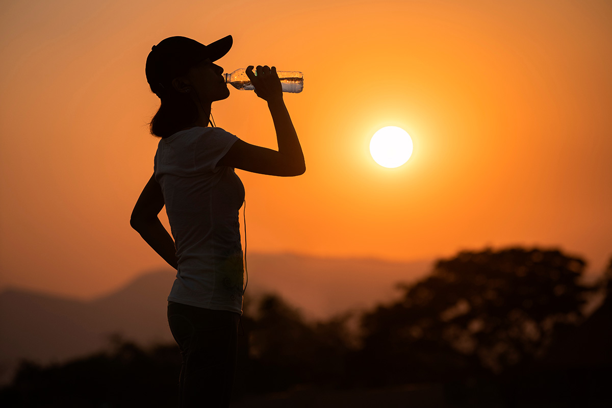 Woman drinking from a water bottle after jogging outdoors at sunset. (Adobe Stock │ #417769340 - tanatat)