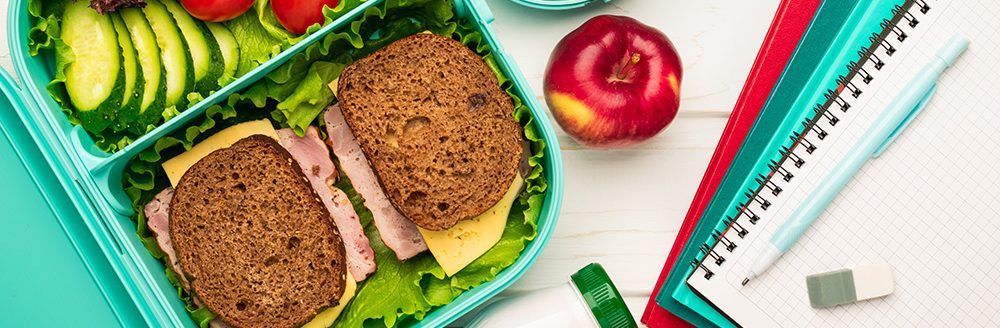 School lunch box with sandwiches and fruit vegetables and school supplies. (Adobe Stock │ #327657911 - SerPhoto)