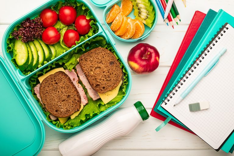 School lunch box with sandwiches and fruit vegetables and school supplies. (Adobe Stock │ #327657911 - SerPhoto)