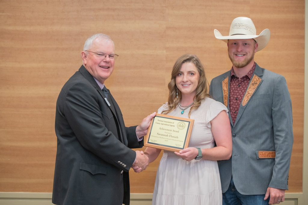 New Mexico State University Hidalgo County Cooperative Extension Service Program Director Savannah Daniels, center, was recognized as the national achievement award winner at the National Association of County Agricultural Agents Annual Meeting and Professional Improvement Conference. Past NACAA President Scott Jensen, left, presented to the award to Daniels, who was accompanied by her husband, Trey Daniels. (Courtesy photo)