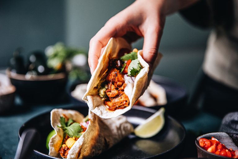 Close-up of a woman serving vegan tacos. Female hand cooking Mexican tacos on kitchen. (iStock │ #1241879697 - alvarez)