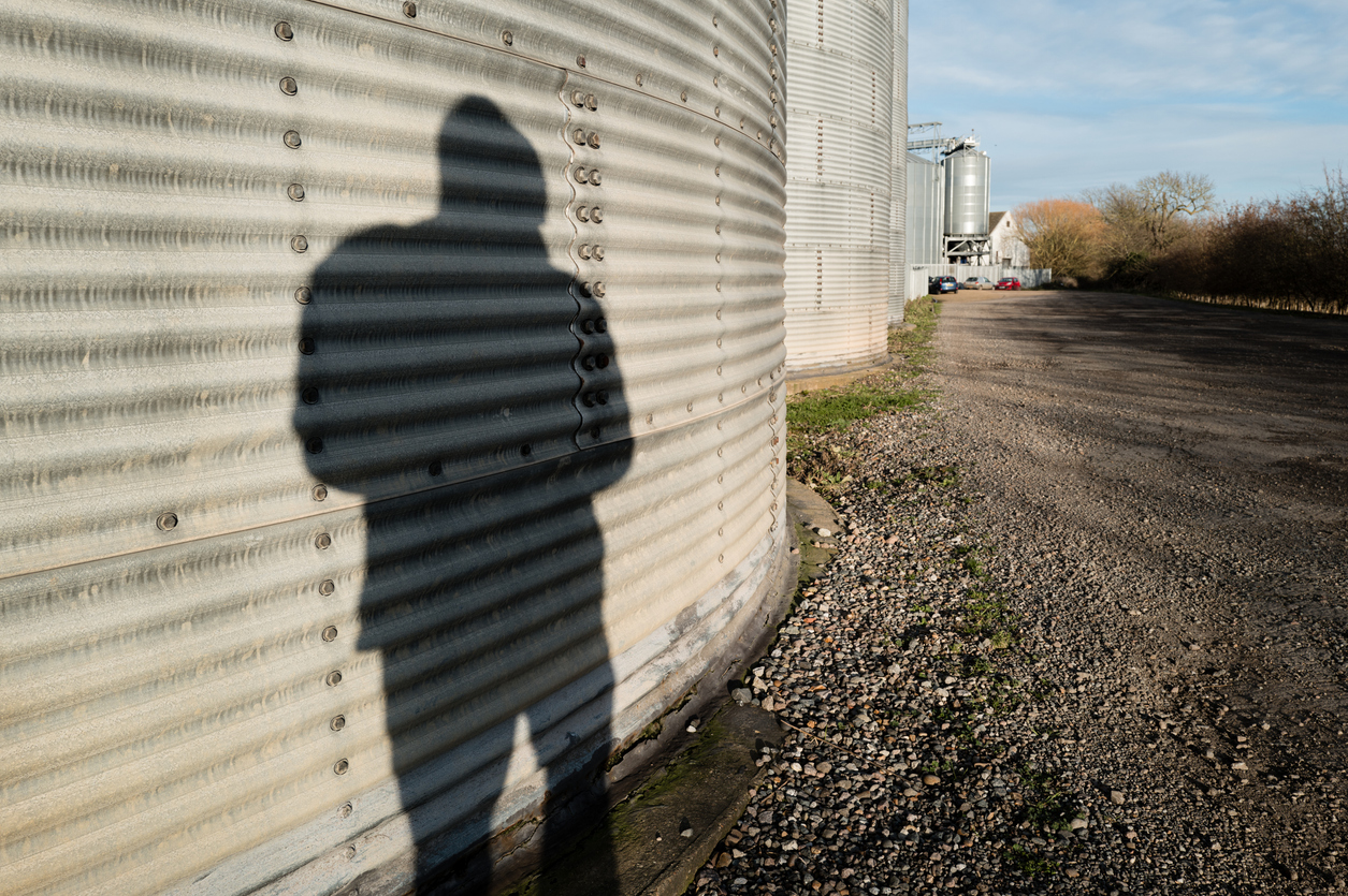 Concept image of a dark shadow of a would-be thief around agricultural grain silos. (iStock │ #1947261562 - Nickbeer)