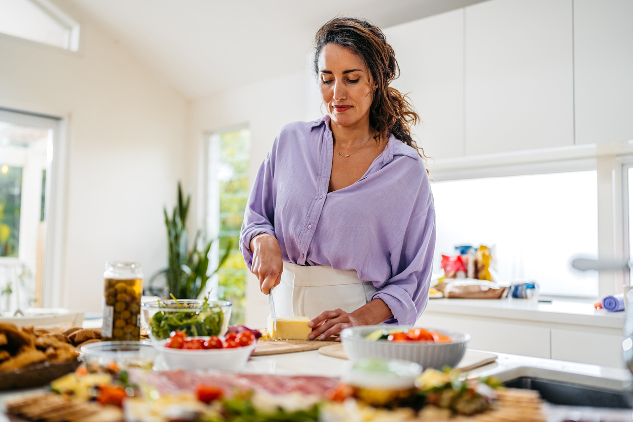Woman cutting cheese while preparing meals in the kitchen. (iStock │ #2190404453 - urbazon)