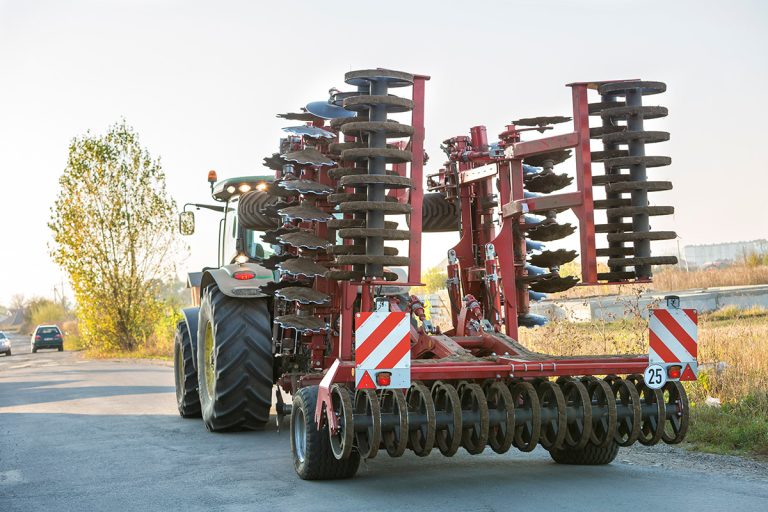 Tractor with disc harrows driving along rural road. (Adobe Stock │ #249348787 - bilanol)
