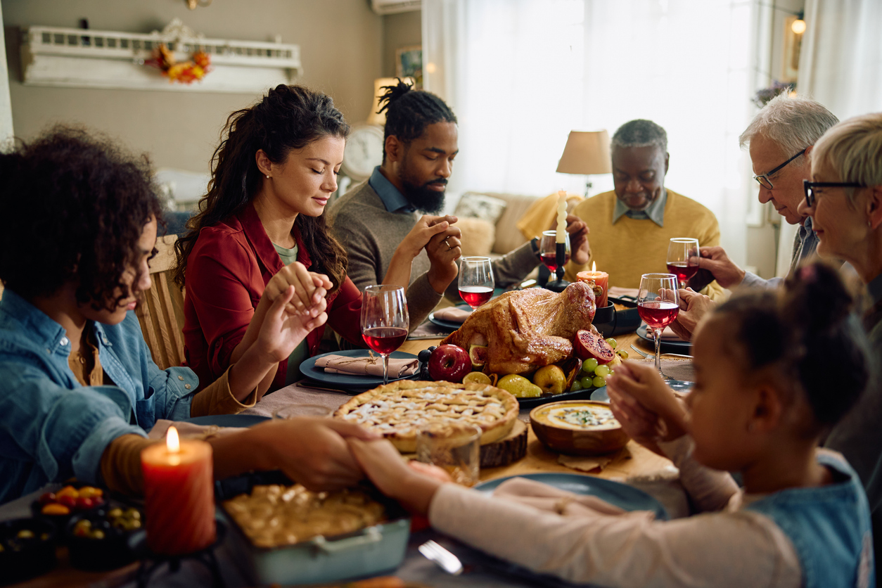 Grateful multigeneration family holding hands while praying at dining table on Thanksgiving. (iStock │ #1727472895 - Drazen Zigic)