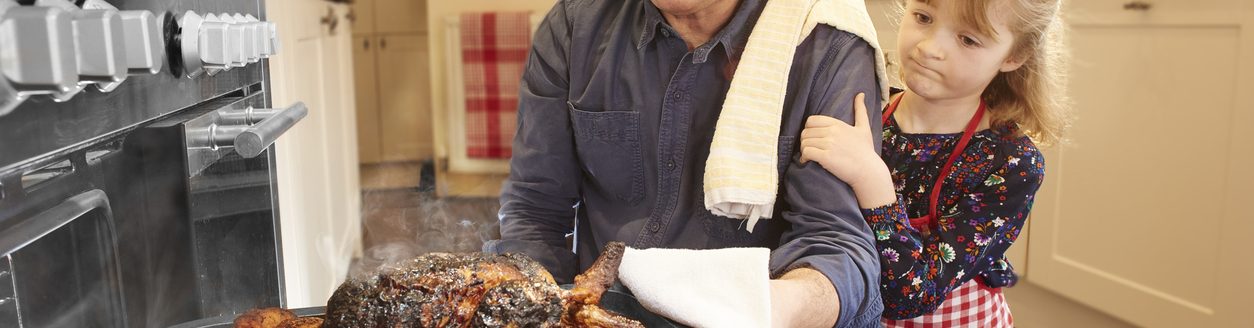 A man pulls the turkey out of the oven only to find it burnt and ruined. His little daughter consoles him. (iStock │ #643548552 - sturti)