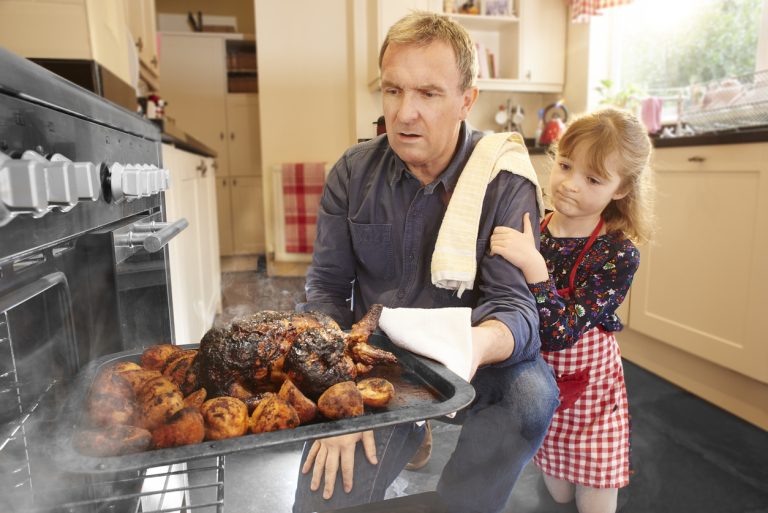 A man pulls the turkey out of the oven only to find it burnt and ruined. His little daughter consoles him. (iStock │ #643548552 - sturti)