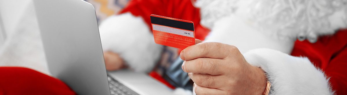 Santa Claus with credit card and laptop on couch at home. (Adobe Stock │ #123565211 - Africa Studio)