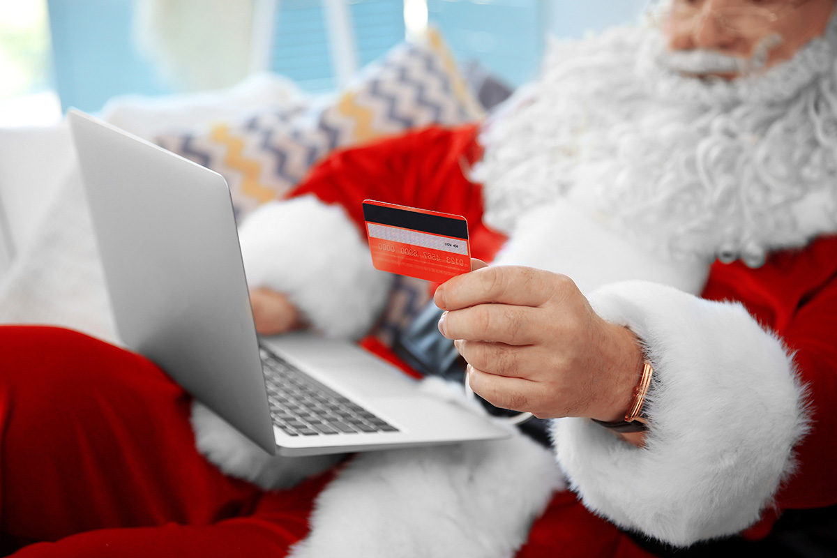 Santa Claus with credit card and laptop on couch at home. (Adobe Stock │ #123565211 - Africa Studio)