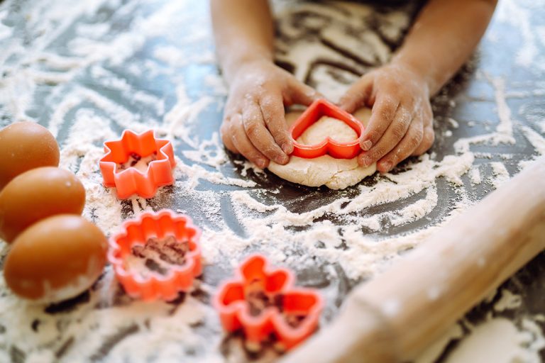Close up of boy hands carving dough with cookie heart cutters. (Adobe Stock │ #409674758 - maxbelchenko)