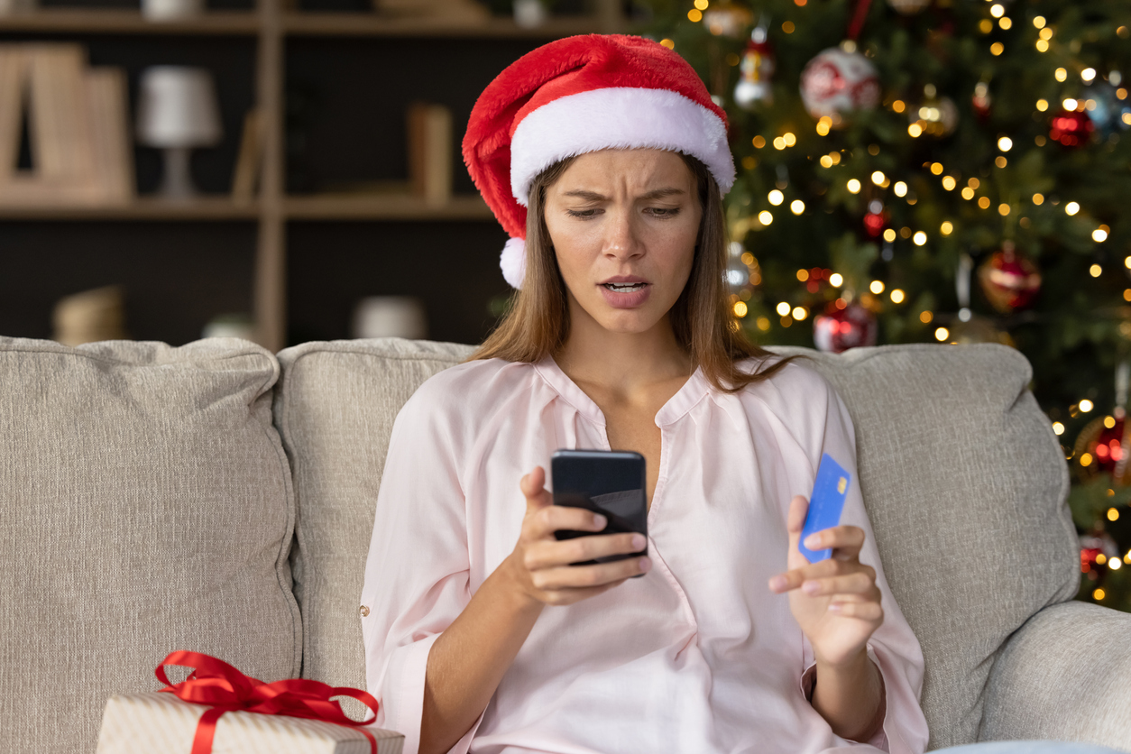 Worried concerned girl in Christmas Santa hat having problems with payment by credit card online for New Year purchases, looking at smartphone screen with puzzled face. (iStock │ #1352106053 - fizkes)