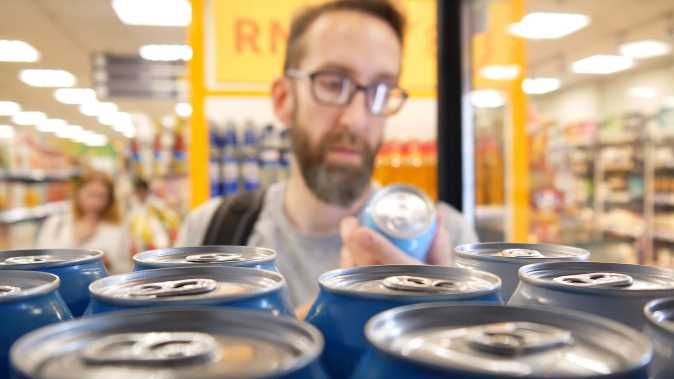 A male buyer examines a drink can from a store fridge. (iStock │ #2160701515 - Stockah)