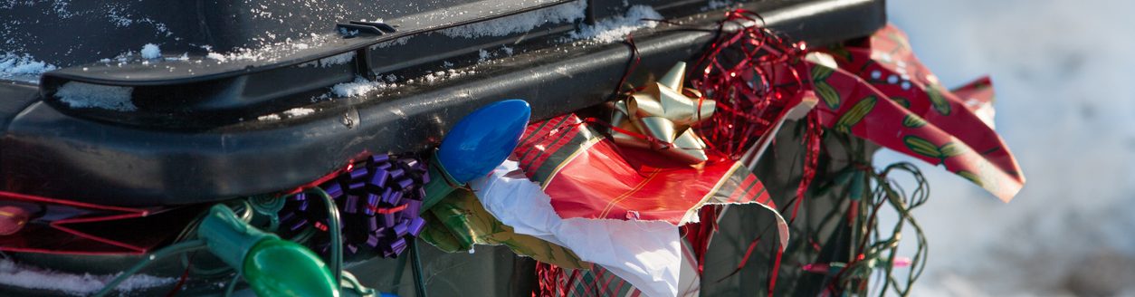 A large plastic trashbin overflowing with garbage and discarded Christmas paper, lights, bows, etc. (iStock │ #462582085 - Allkindza)