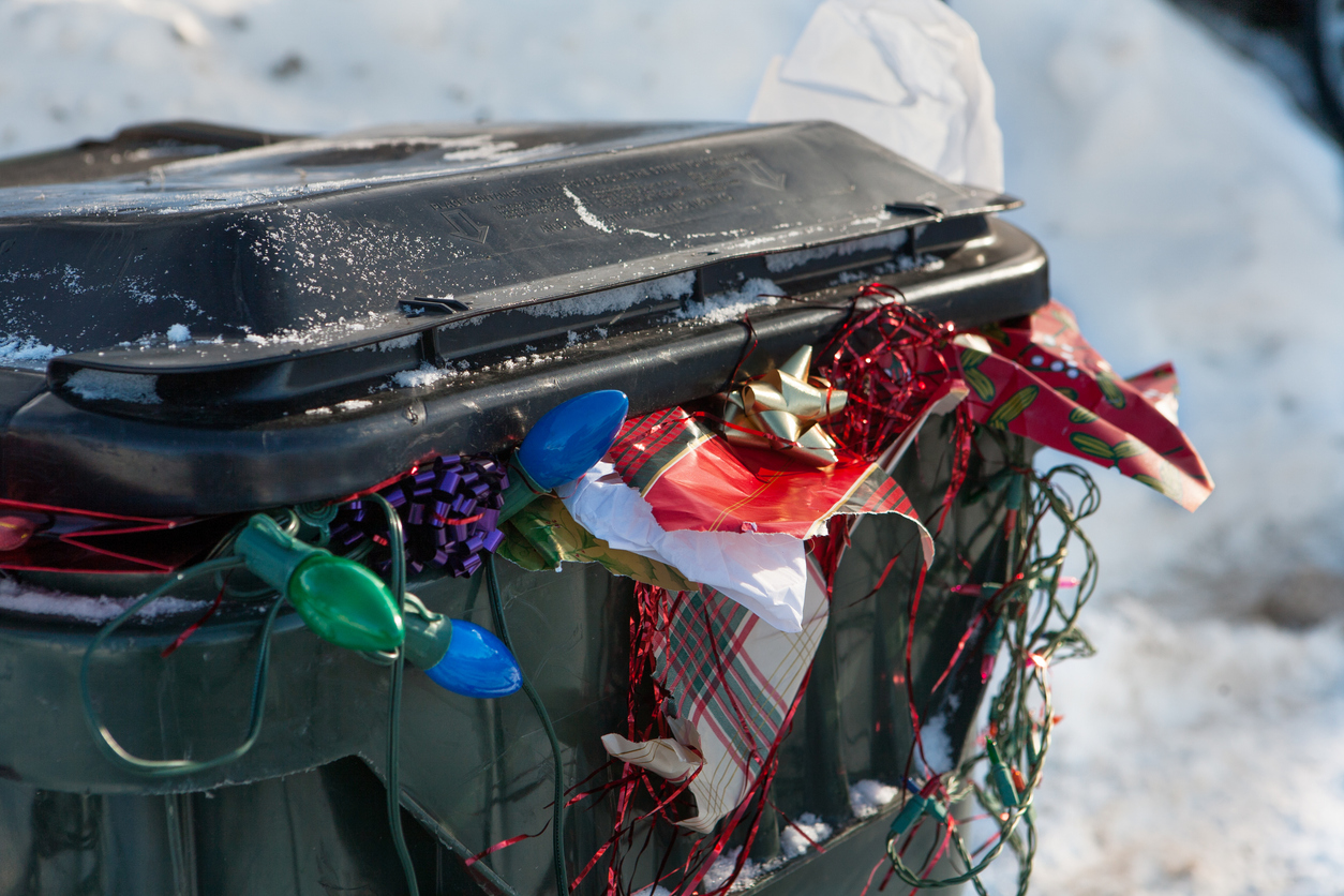 A large plastic trashbin overflowing with garbage and discarded Christmas paper, lights, bows, etc. (iStock │ #462582085 - Allkindza)