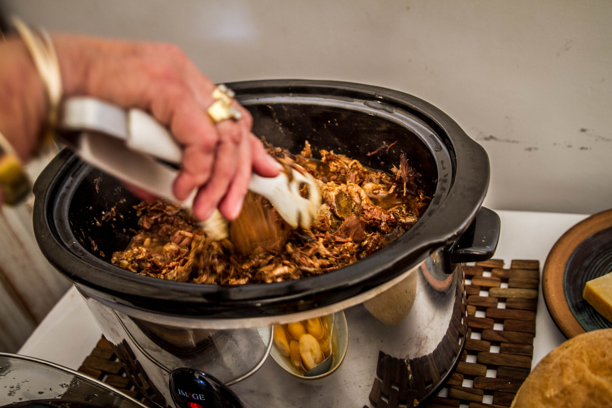 Leg of lamb in stainless steel slow cooker with hand string the pot. (iStock │ #464922016 - FredaRoetjens)